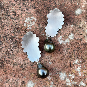 silver flower inspired earrings with black pearl drop on a brick background