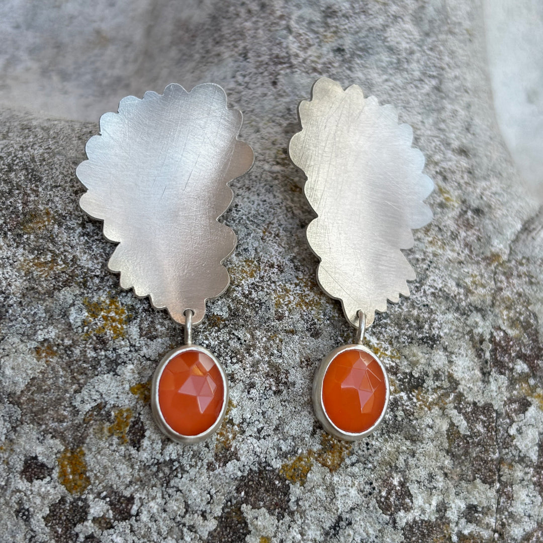 silver flower inspired earrings with a carnelian drop on a stone background