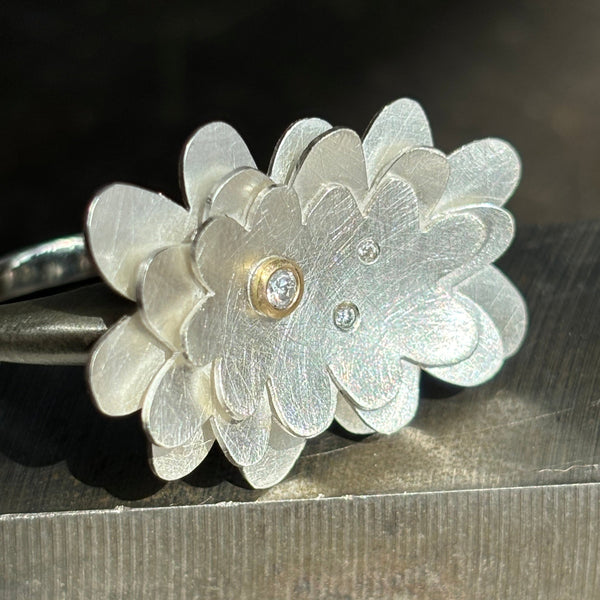 sterling silver abstract flower ring with three diamonds, one set in gold, on a steel background