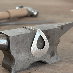 textured silver pendant on an anvil on a workbench