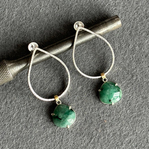 Silver hoop earrings with green gemstones on a gray surface