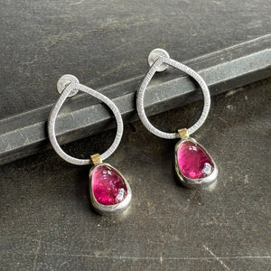 Pair of silver hoop earrings with pink gemstones on a dark surface