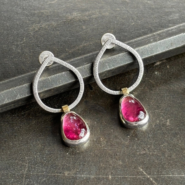 Pair of silver hoop earrings with pink gemstones on a dark surface