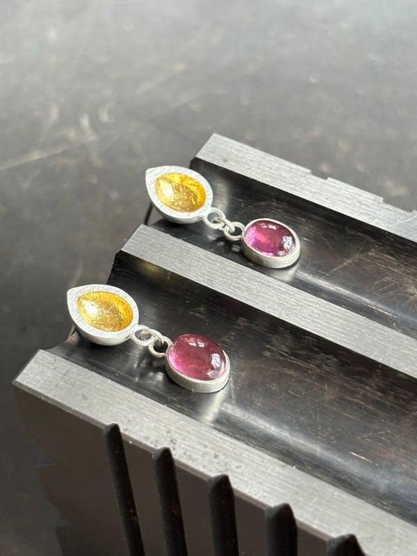 silver and gold seed pod earrings with tourmaline drops on a swage block