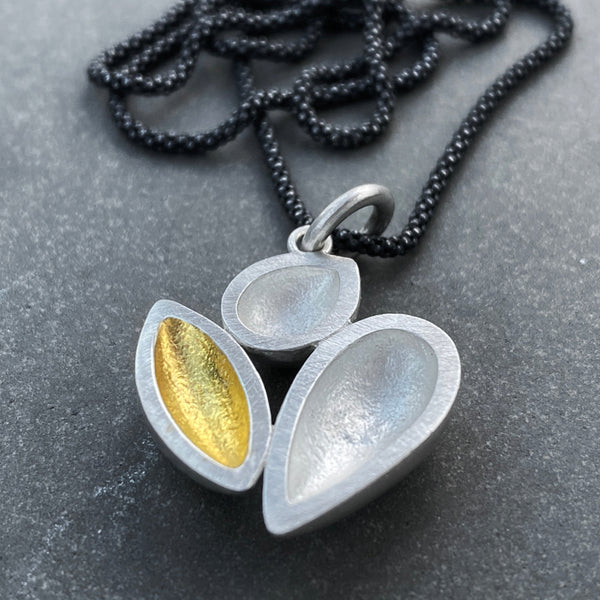 sterling silver pendant with three elements, one of which has 24k gold keum boo, hanging from an oxidised chain, on grey background