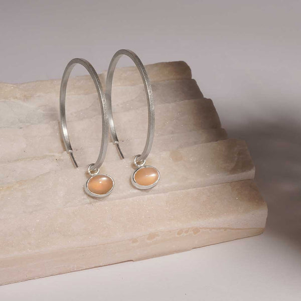 sterling silver hoop earrings with peach moonstone drop on a tile